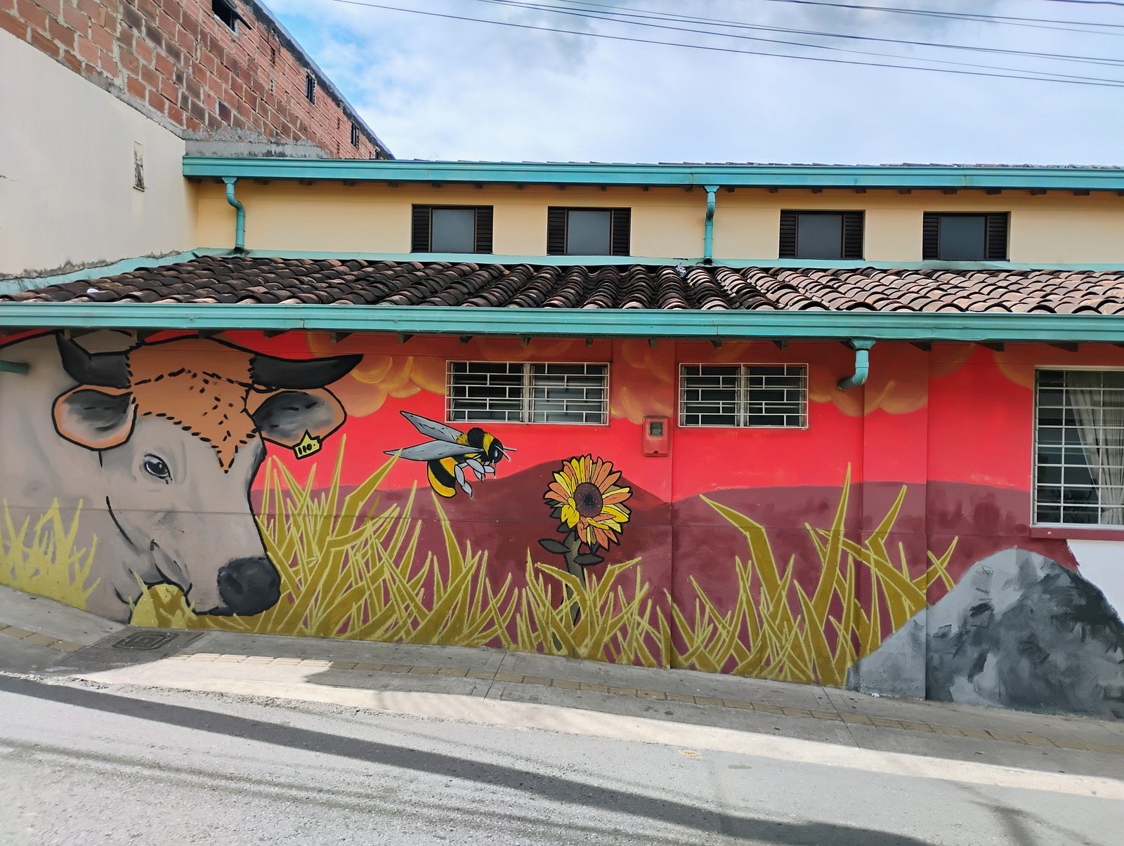 Mural de una vaca, una abeja y un girasol pintado a lo largo de un muro.