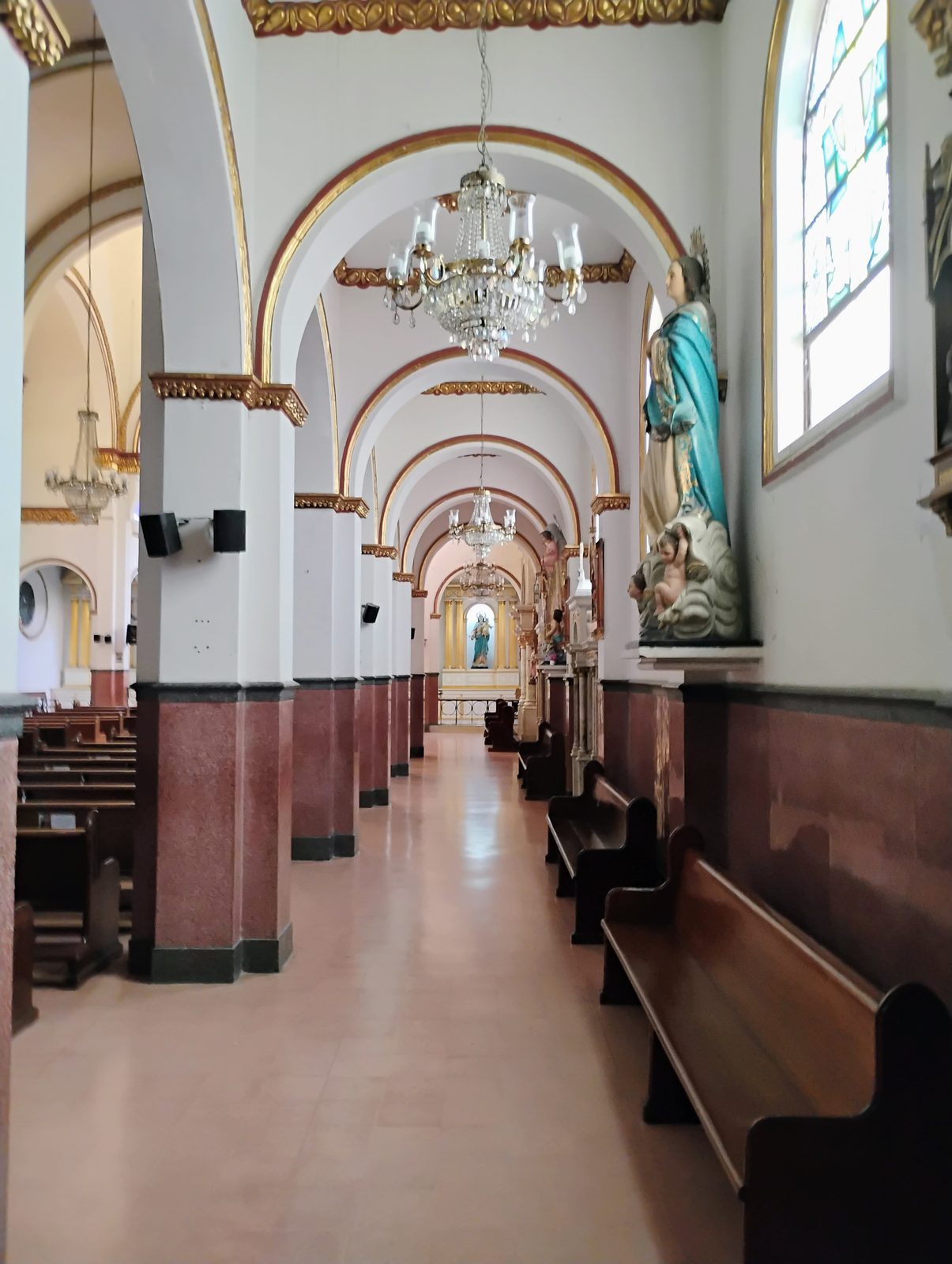 Nave lateral del templo, con arcos dorados, vitral y bancas de madera.